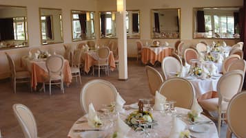 A banquet hall with multiple round tables set for dining, each with white tablecloths and floral centerpieces.