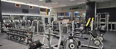 Une salle de sport équipée de divers appareils d’entraînement, notamment des tapis de course, des appareils de musculation et des poids libres.