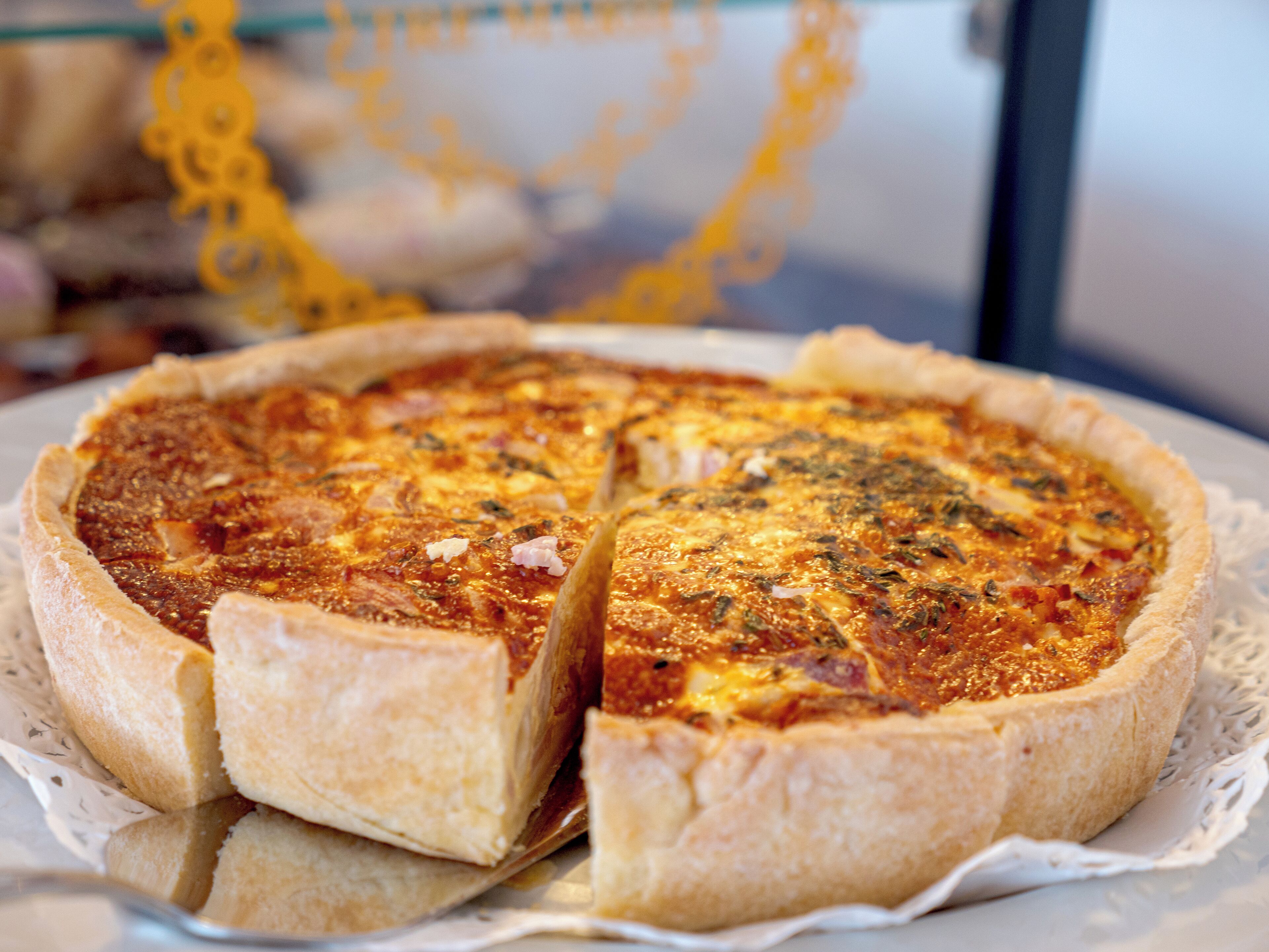 Una quiche con una porción faltante, sobre un plato blanco con un encaje.
