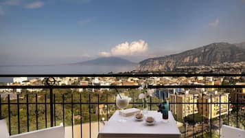 Un balcón con mesa lista para comer, con vistas a un paisaje urbano y una montaña al fondo.