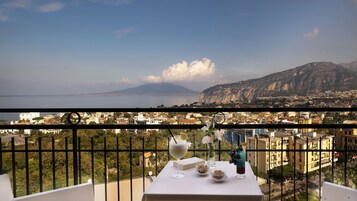 A balcony with a table set for dining, overlooking a cityscape with a mountain in the distance.