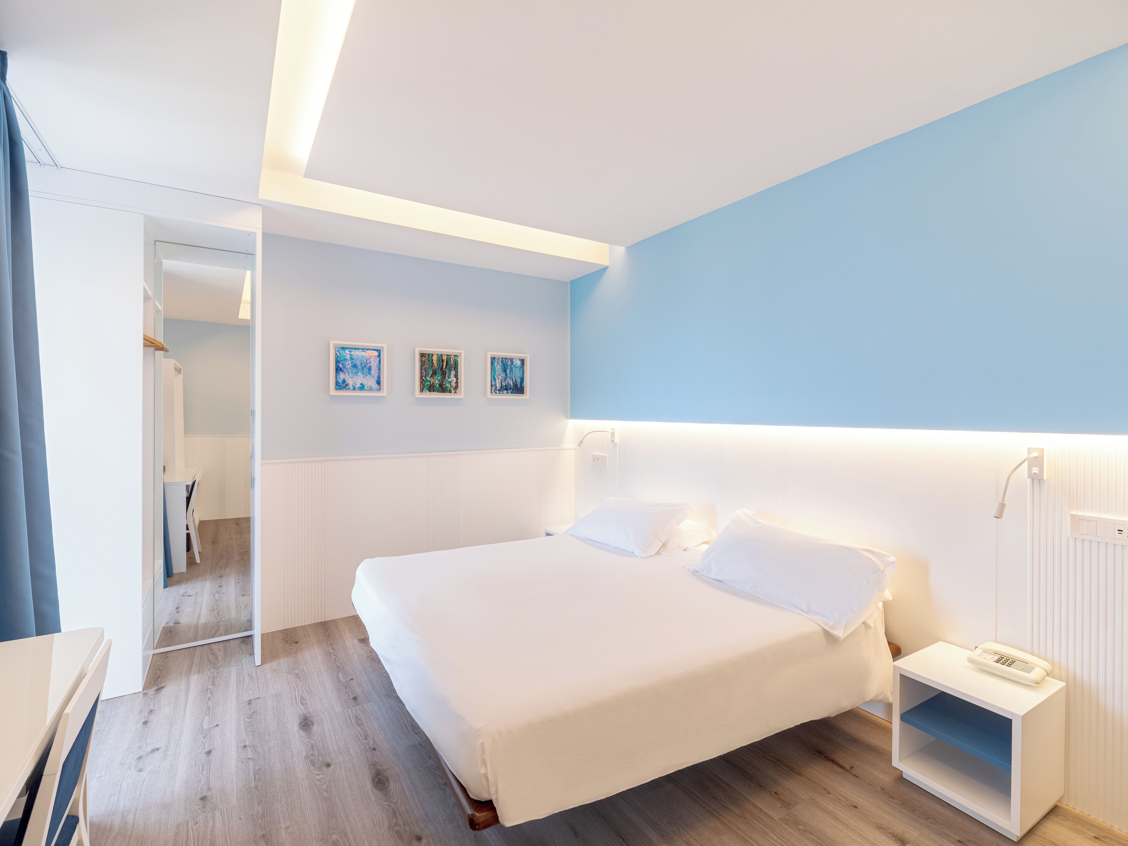 Quarto de hotel moderno com cama grande, mesa de cabeceira e obra de arte na parede.