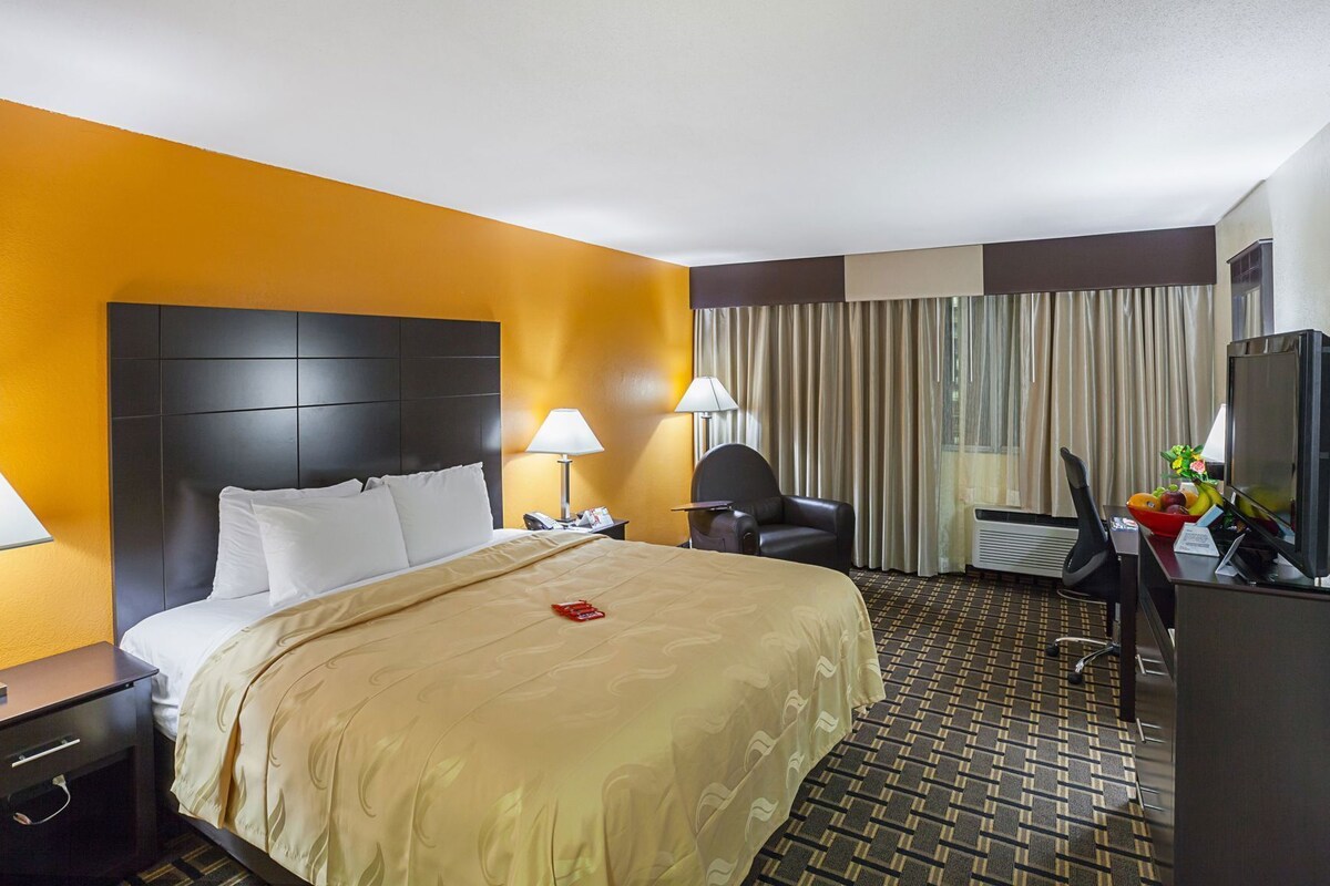 A hotel room with a bed, two bedside tables, a desk with a chair, a television, and a window with curtains.