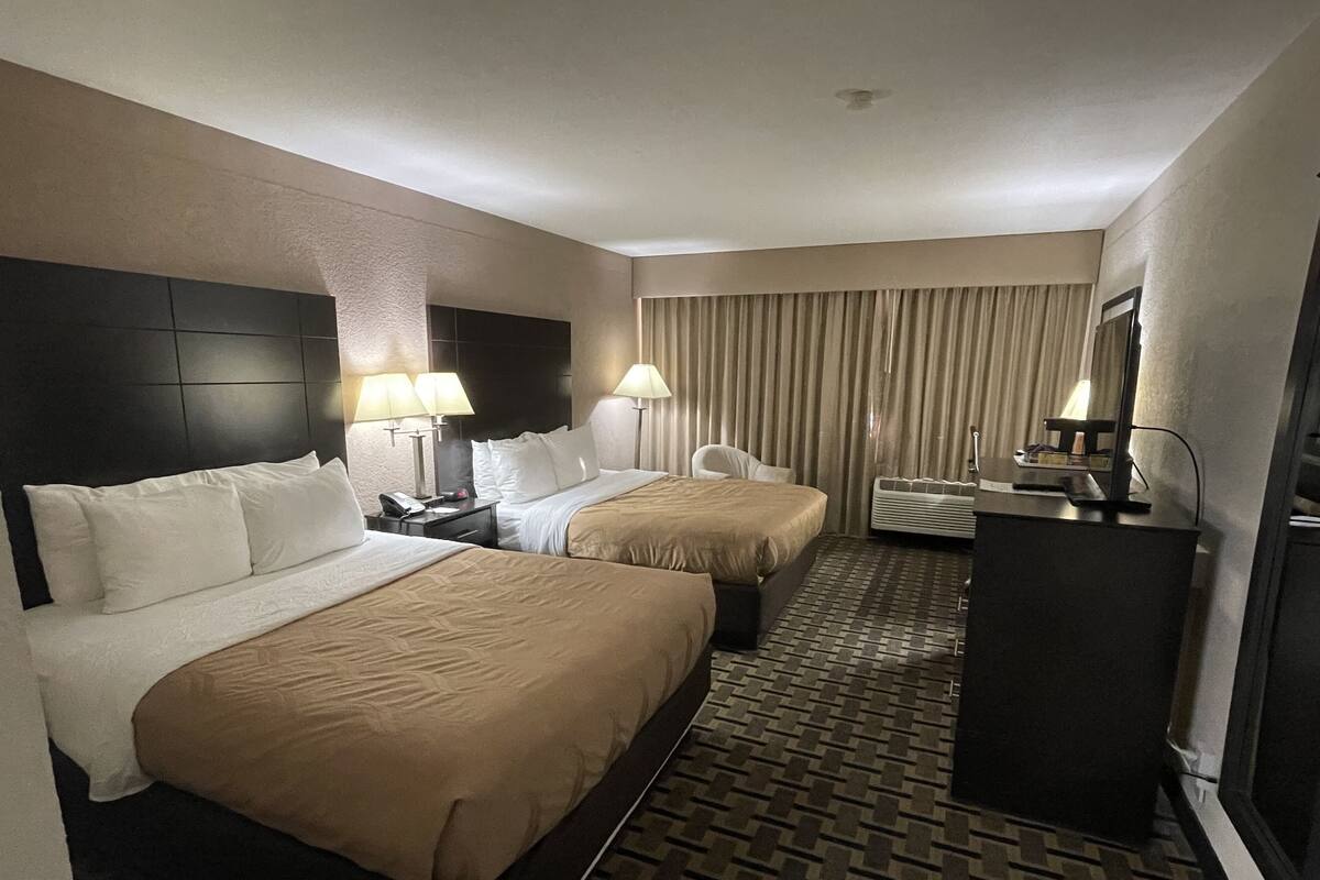 Quarto de hotel com duas camas, uma escrivaninha, uma cadeira e um minibar.