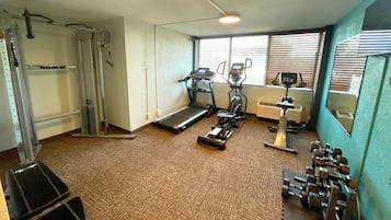 A gym with a treadmill, elliptical, weight bench, and free weights.