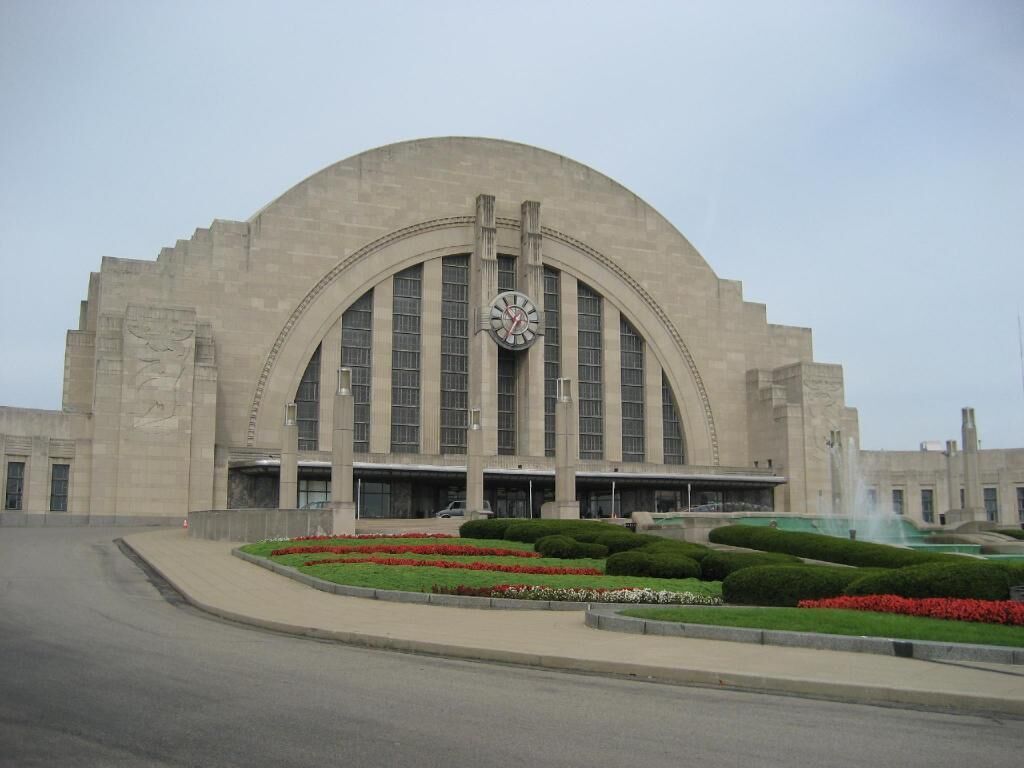 A large building with a prominent clock, arched windows, and a landscaped garden in front.