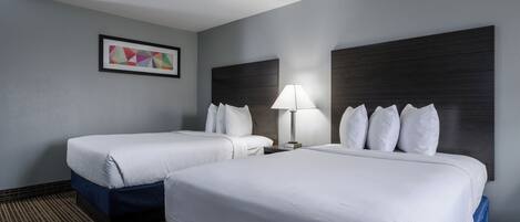Habitación de hotel con dos camas, una mesita de noche, una lámpara y un cuadro en la pared.