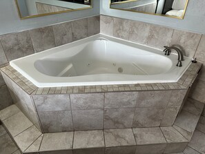 A corner bathtub with a white finish, tiled walls, and a corner mirror.