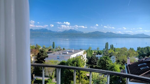 A view of a lake with mountains in the background, buildings in the foreground, and a clear sky.
