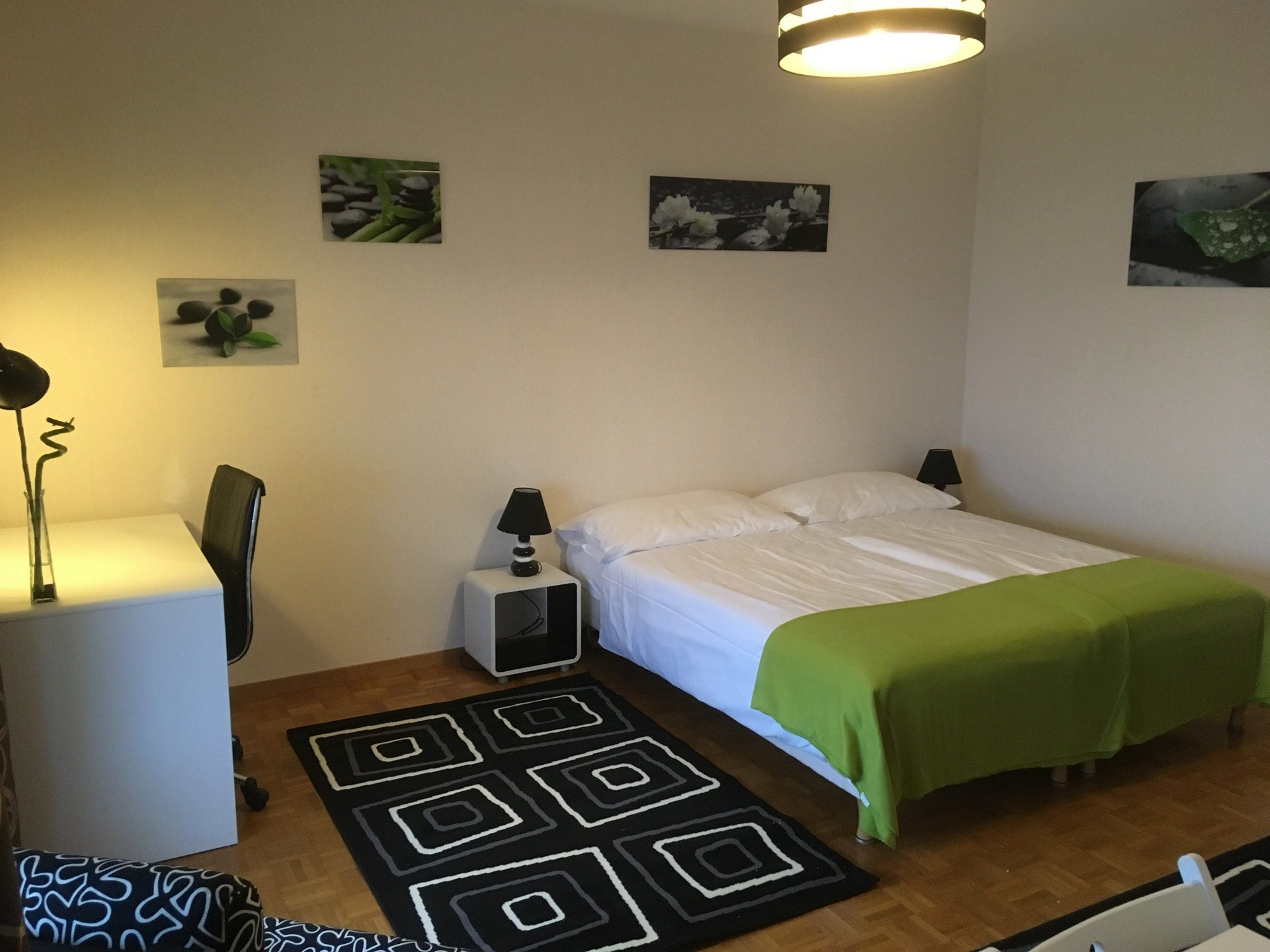 Un dormitorio ordenado con cama, mesita de noche, lámpara y una pequeña alfombra.
