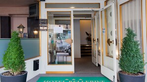 A hotel entrance with a green carpet reading "HOTEL BELLERIVE BIENVENUE," potted plants, and a glass door leading inside.