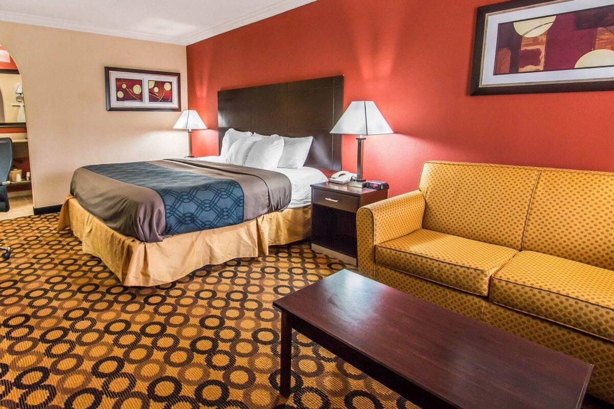 Een hotelkamer met een bed, een slaapbank, een nachtkastje met lamp en een kamerbreed tapijt met dessin.