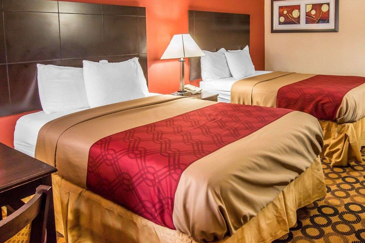 Een hotelkamer met twee bedden, een nachtkastje, een lamp en een lijst aan de muur.