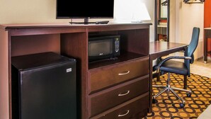 Ett hotellrum med ett skrivbord, en tv, en mikrovågsugn, ett kylskåp, en stol och en mönstrad matta.