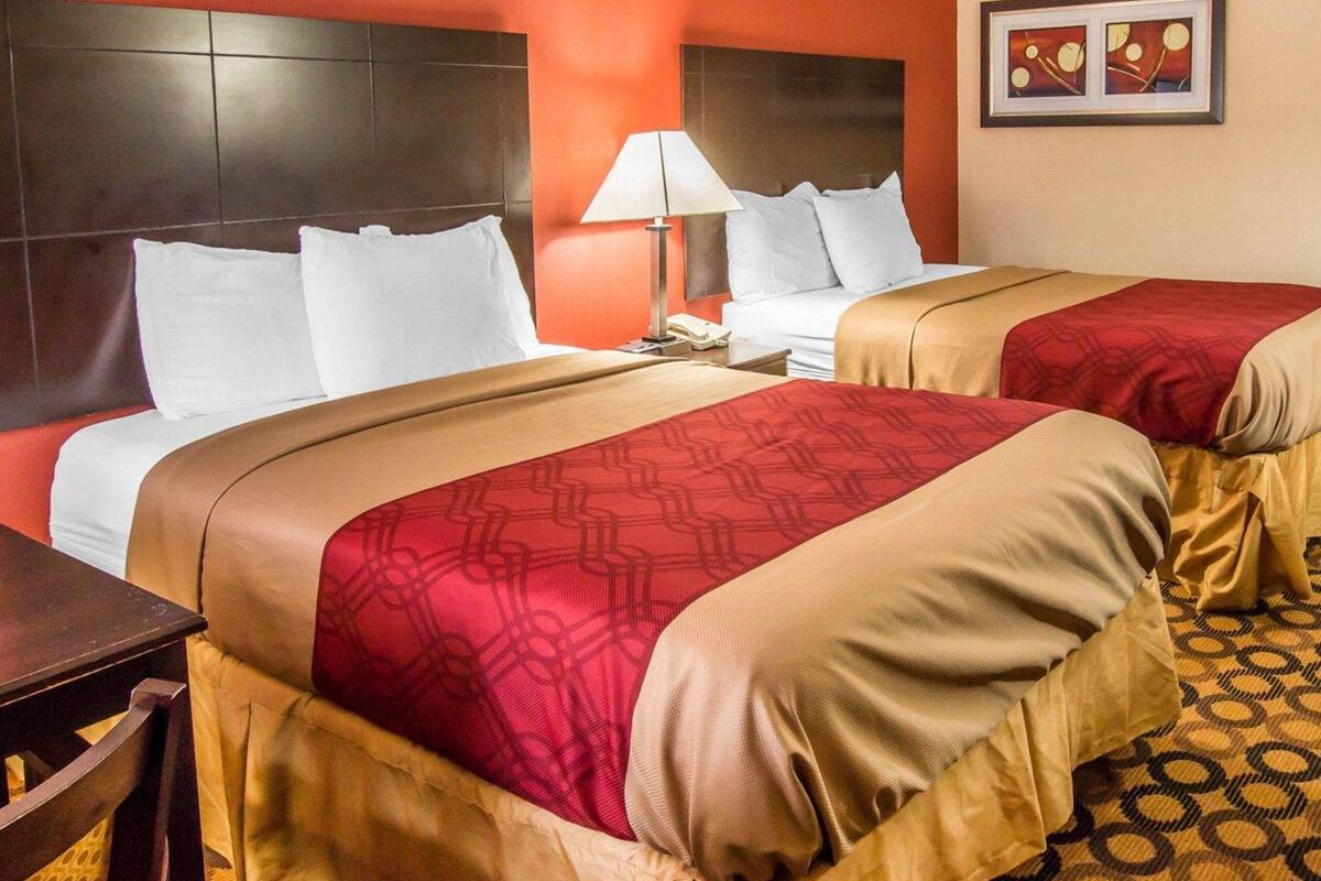 Een hotelkamer met twee bedden, een nachtkastje, een lamp en een lijst met een afbeelding aan de muur.
