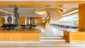 Un hall d’entrée spacieux avec un grand escalier, un comptoir d’accueil et un piano.