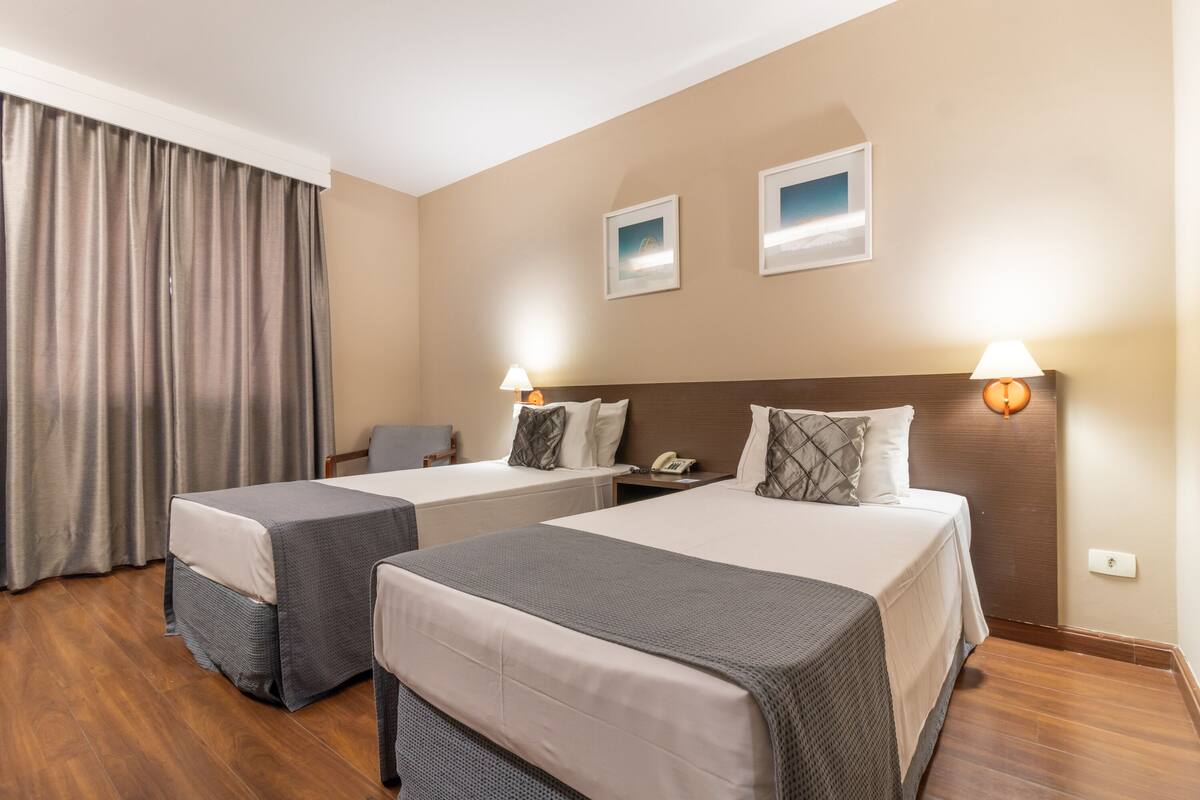 Quarto de hotel com duas camas, uma mesa, uma cadeira e um telefone.