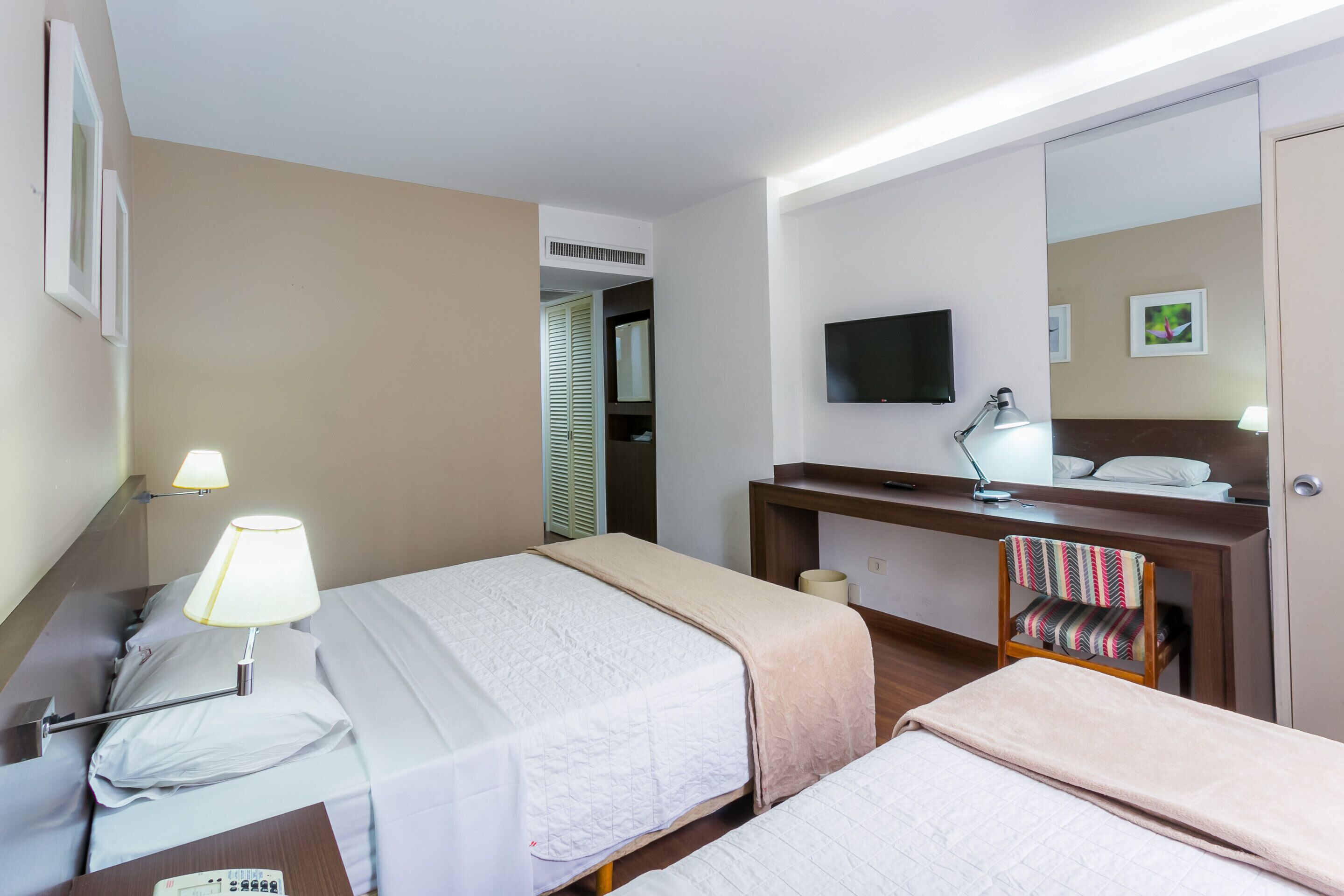 A hotel room with two beds, a desk with a lamp, a television, and a mirror.