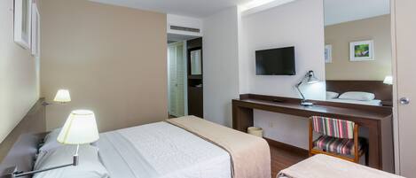A hotel room with two beds, a desk with a lamp, a television, and a mirror.