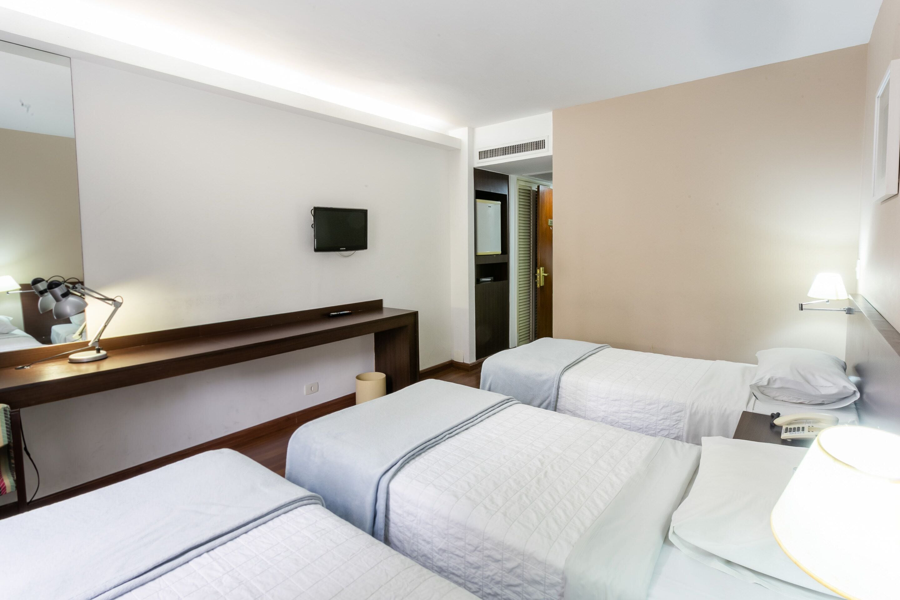 A hotel room with two single beds, a desk with a lamp, a TV, and a bathroom door.