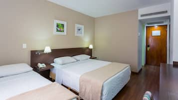 Une chambre d’hôtel avec deux lits, une tête de lit en bois, des lampes de chevet, un téléphone et des tableaux encadrés au mur.