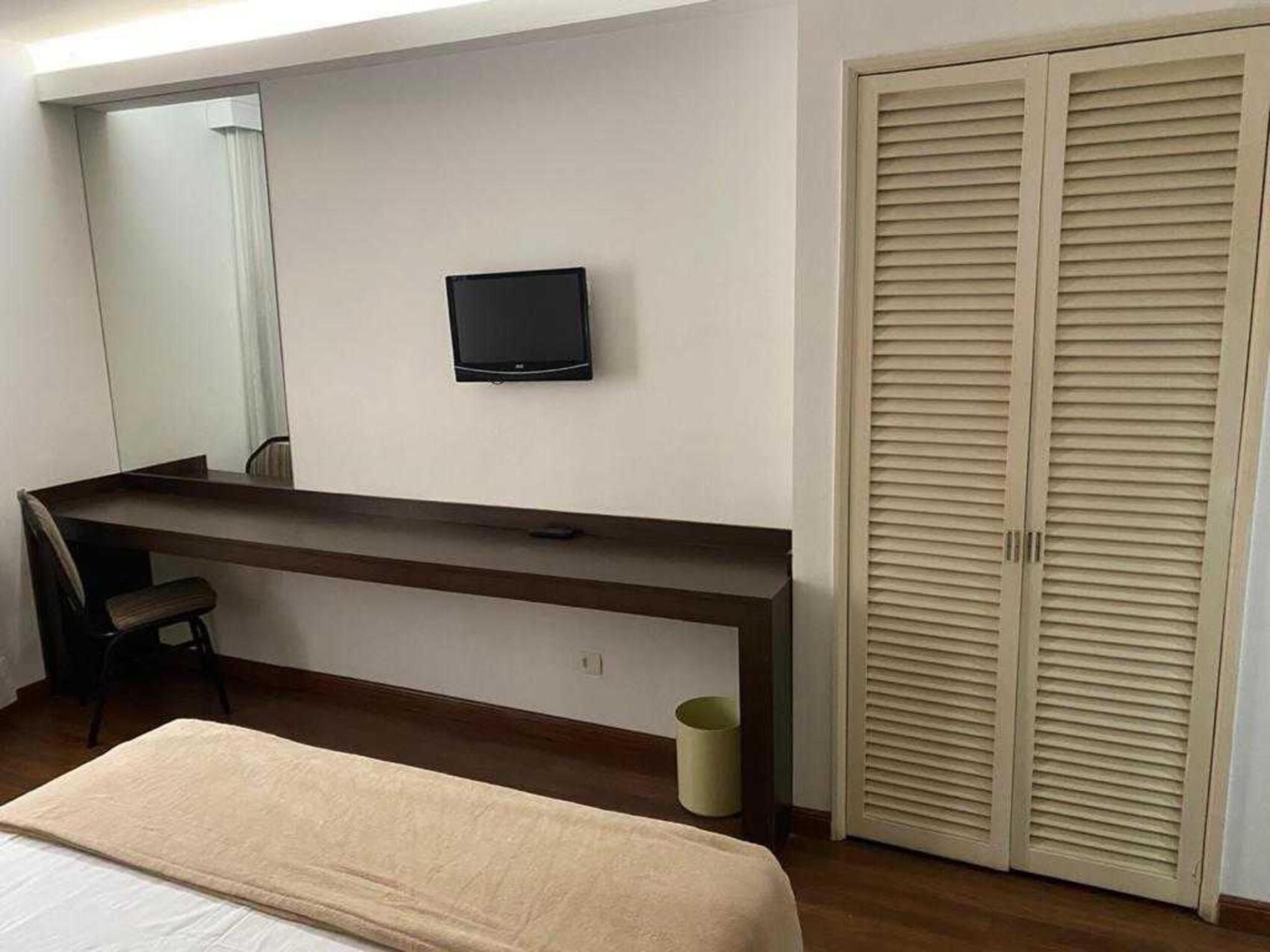 Una habitación de hotel con cama, escritorio, silla, televisor y armario.
