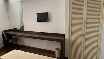 Una habitación de hotel con cama, escritorio, silla, televisor y armario.