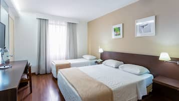 Quarto de hotel com duas camas, uma mesa, uma televisão e janela com cortinas.