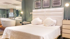 Une chambre d’hôtel moderne dotée d’un grand lit, d’une salle de bain séparée avec baignoire, d’une coiffeuse avec miroir et d’une table de chevet avec lampe.