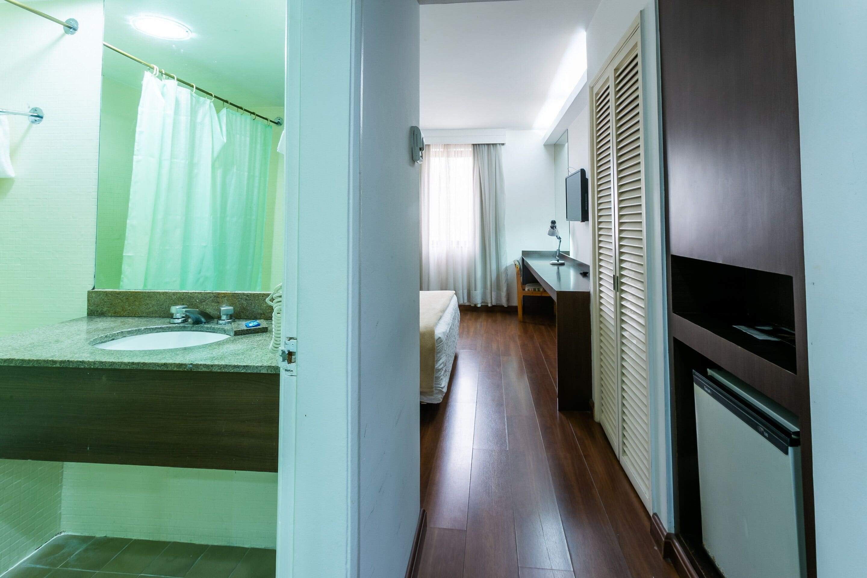 A hotel bathroom with a sink, mirror, and shower curtain.