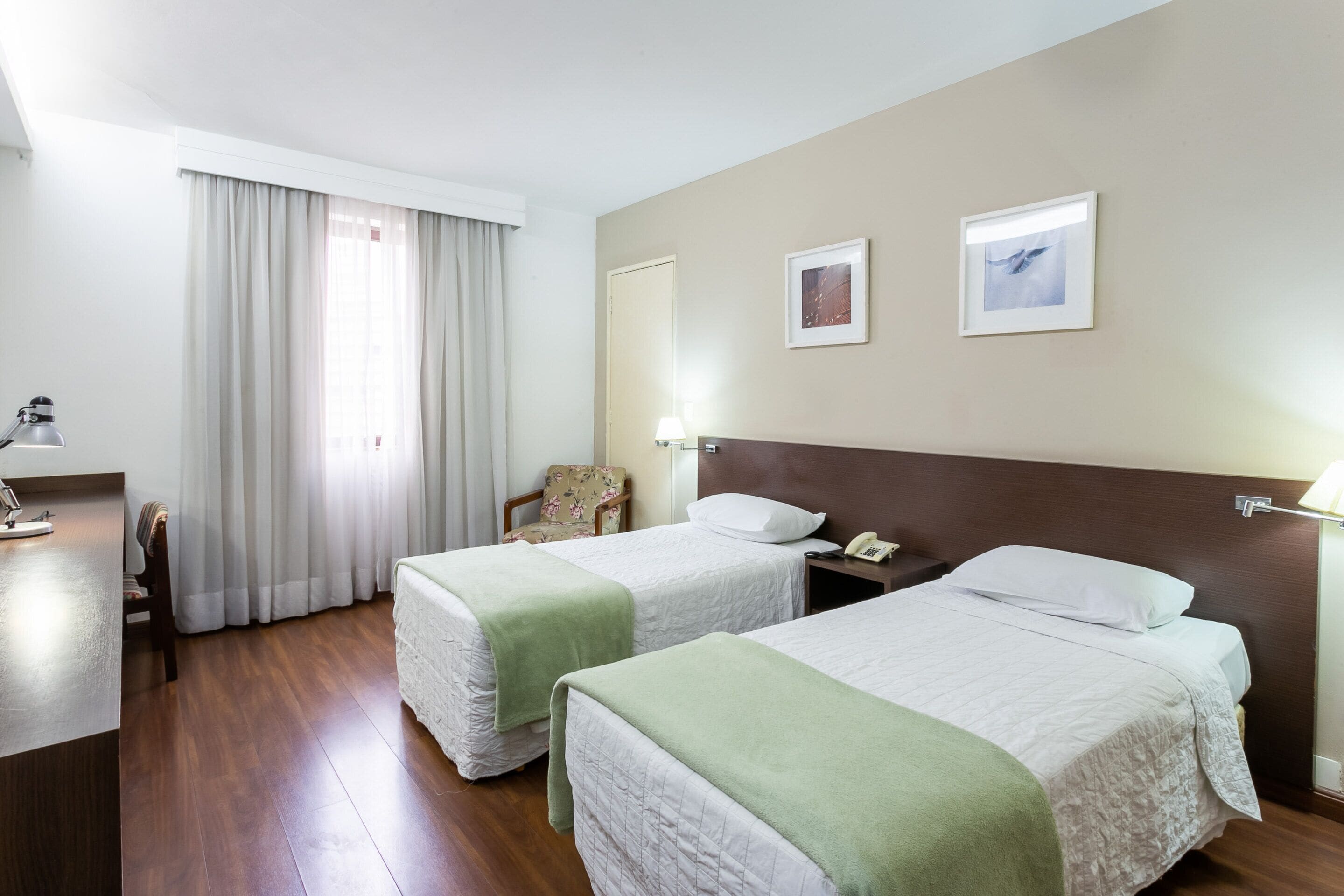 Une chambre d’hôtel avec deux lits, un bureau, une chaise et une fenêtre avec des rideaux.