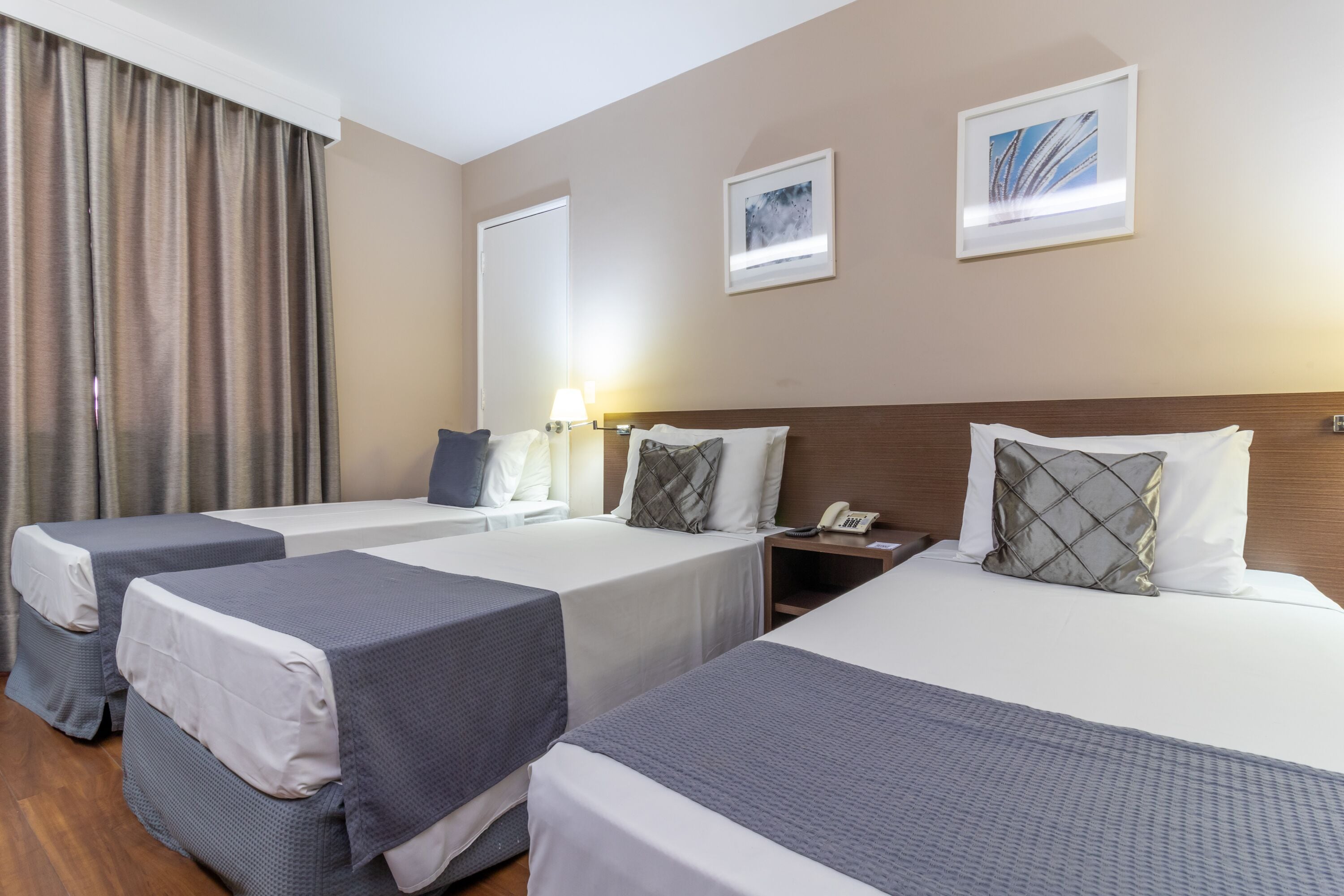 Habitación de hotel con dos camas individuales, una cama doble, una mesita de noche con lámpara y un teléfono.