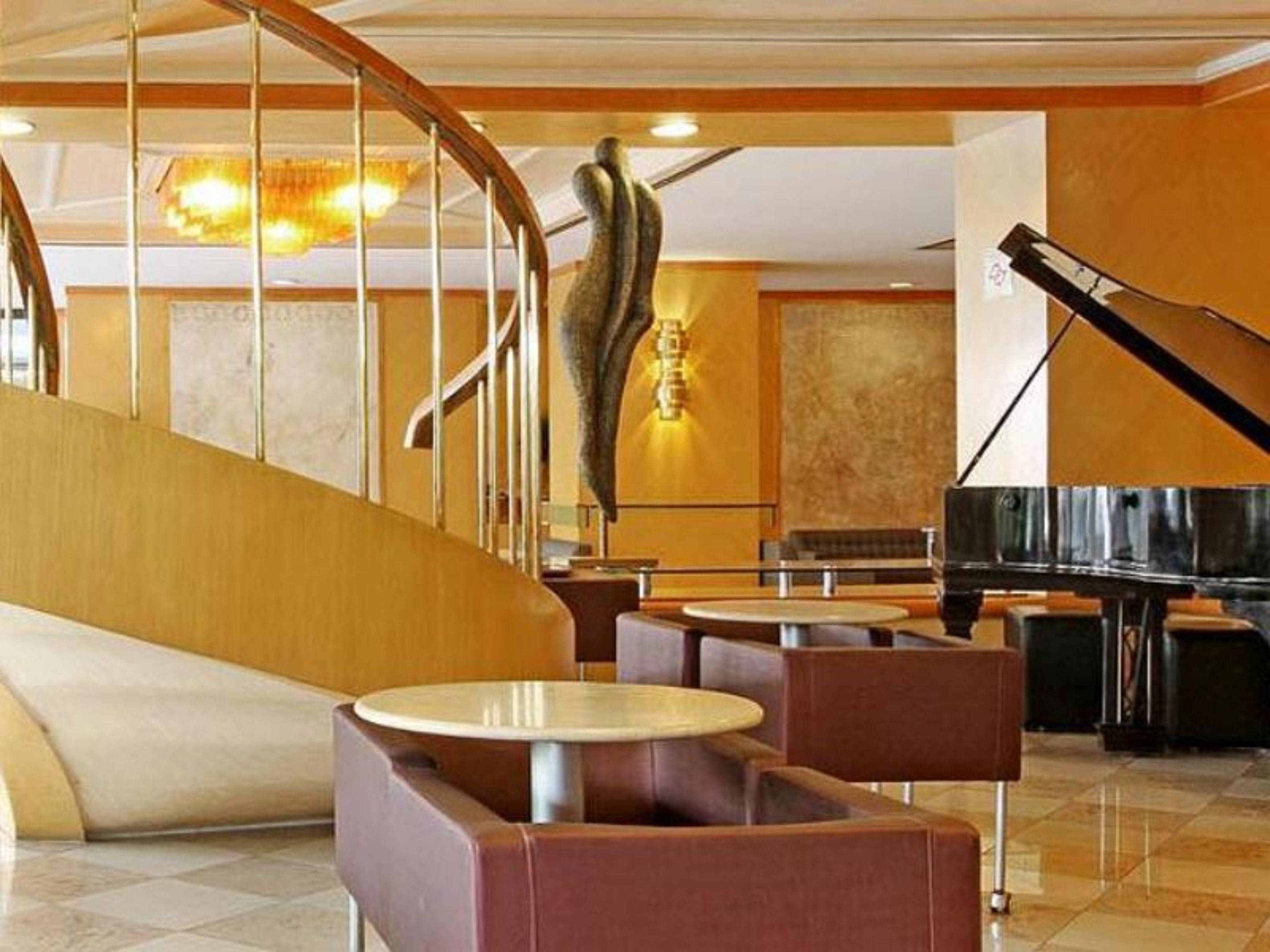 Un hall d’entrée moderne avec un escalier à volutes, des tables rondes et un grand piano.