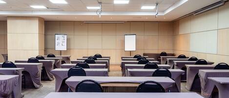 A conference room with multiple tables covered with tablecloths, arranged in rows, and equipped with chairs.