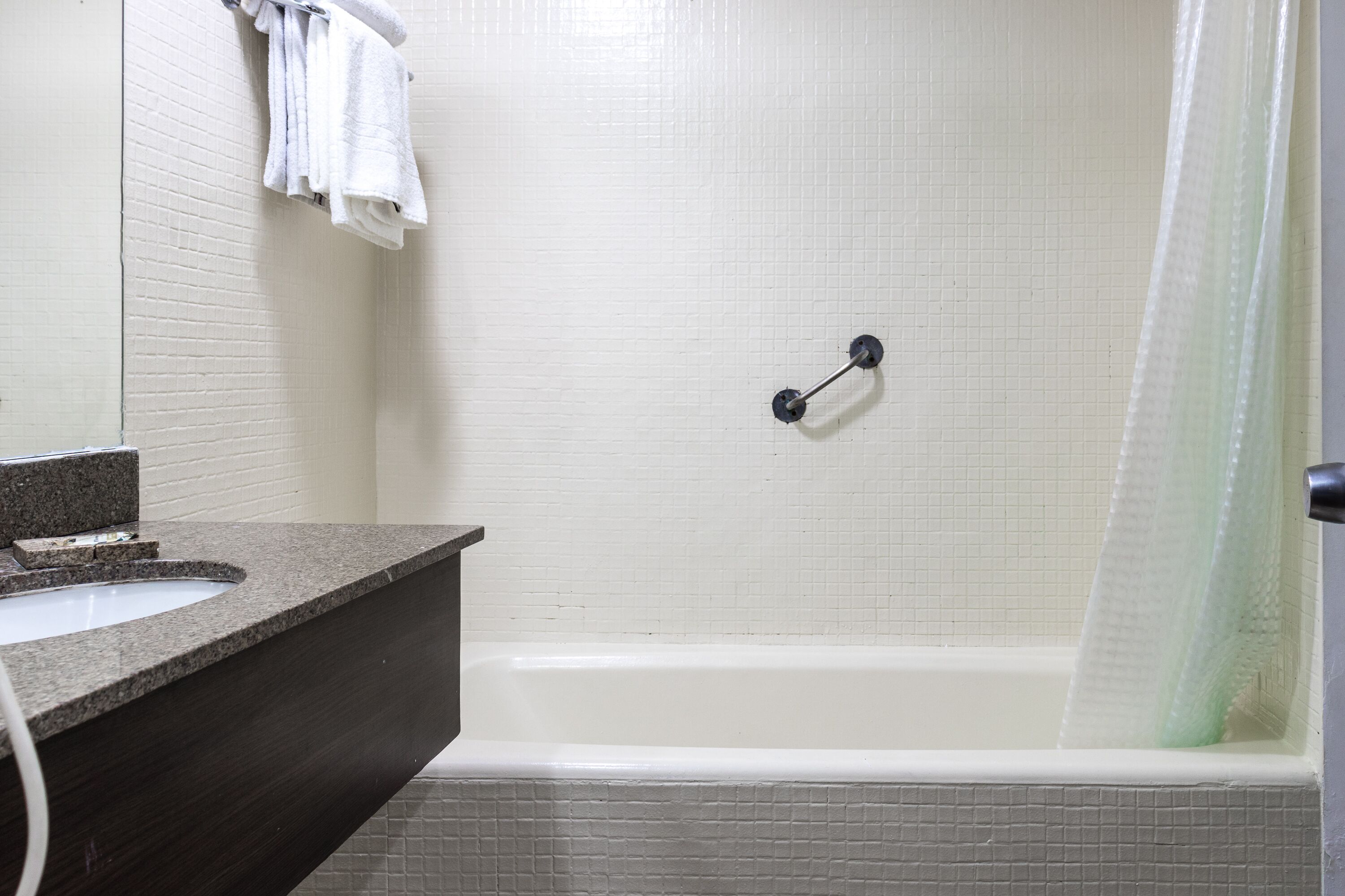 A bathroom with a white tiled wall, a dark granite countertop, a white sink, and a shower with a glass door.