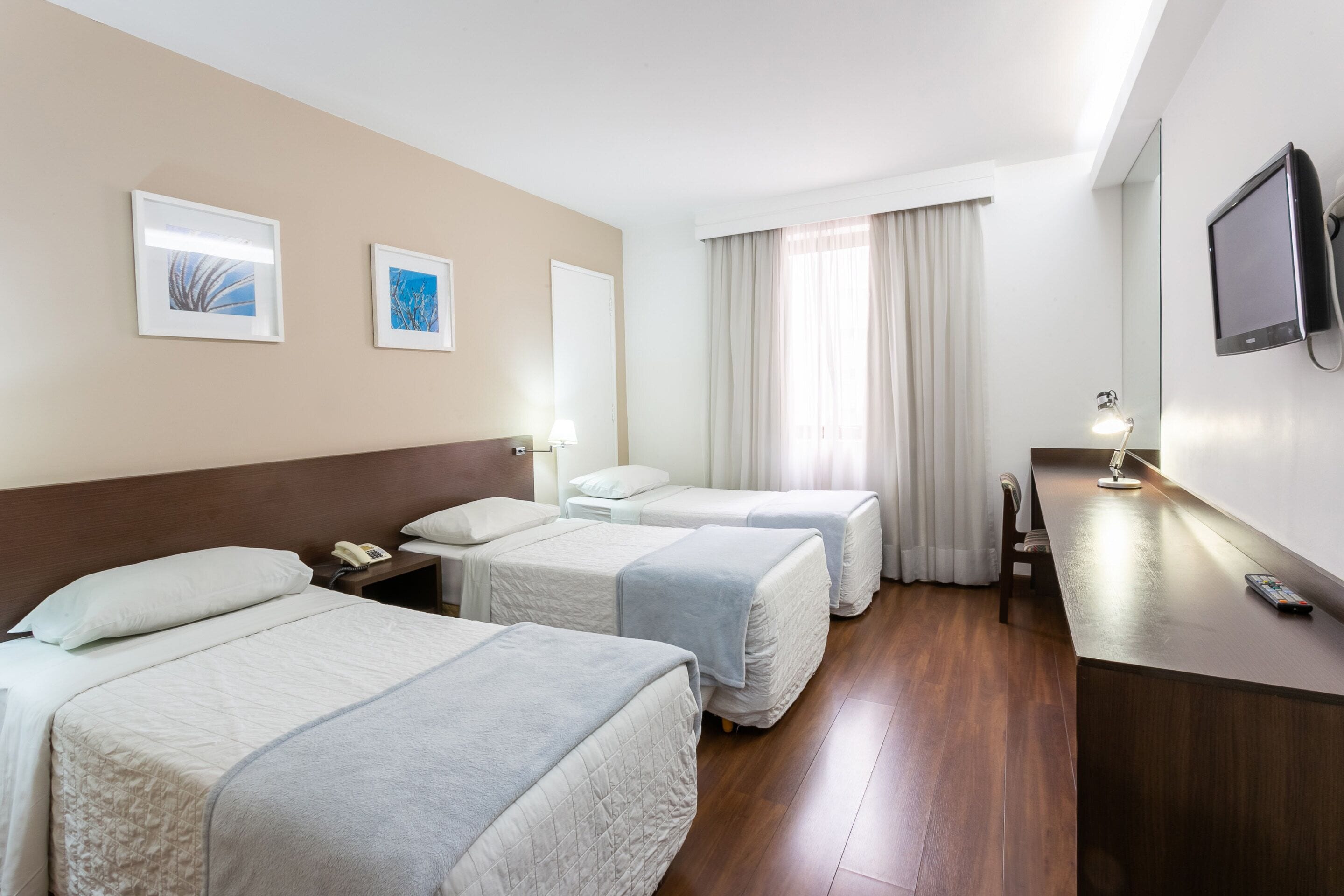 Quarto de hotel com duas camas, uma escrivaninha, televisão e obras de arte nas paredes.