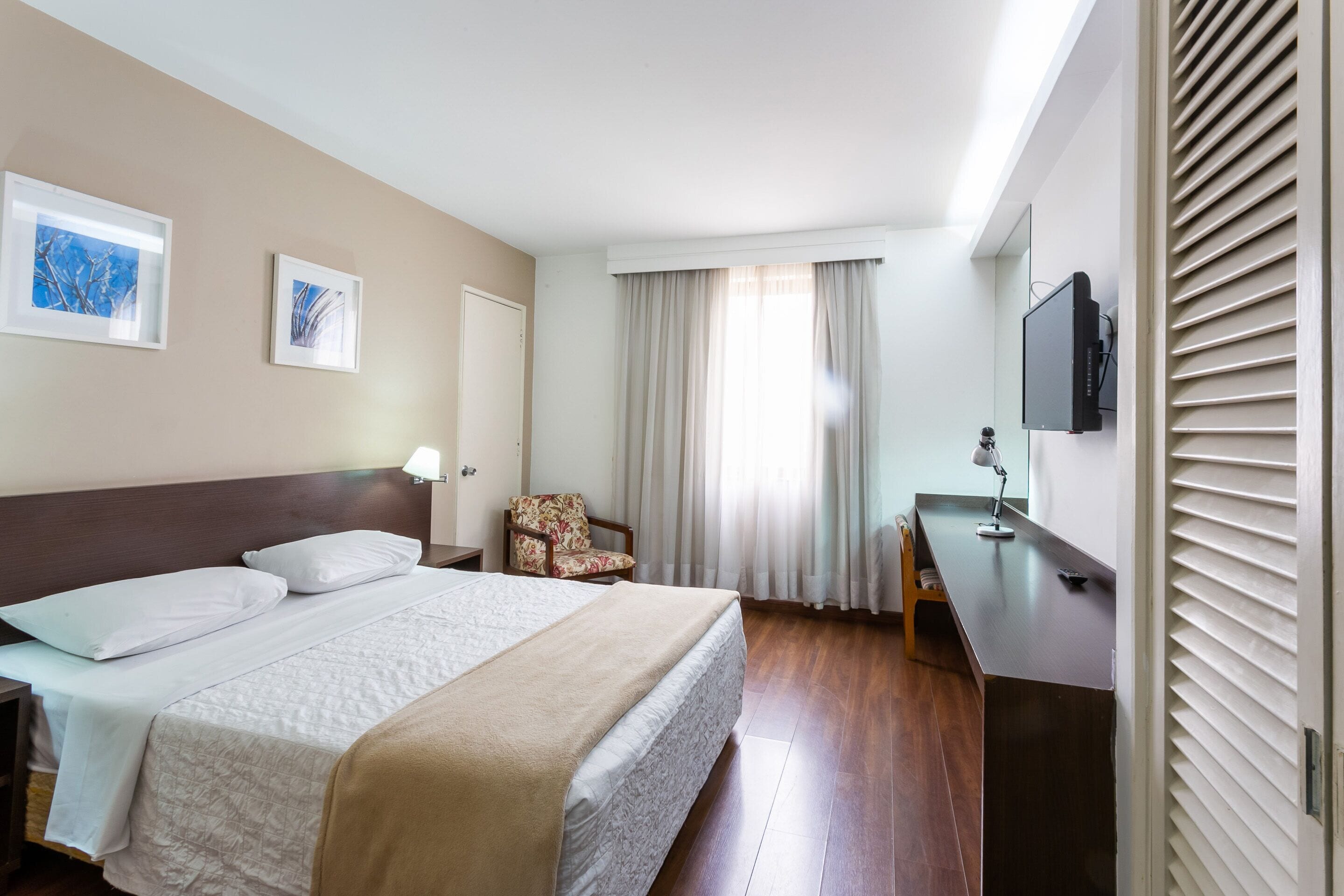 A hotel room with a bed, a desk, a chair, a TV, and curtains.