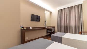 Quarto de hotel com duas camas, uma escrivaninha, uma cadeira, uma TV fixada na parede e uma janela com cortinas.