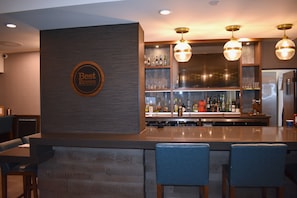 Un espace bar avec un comptoir en bois, des tabourets de bar et une enseigne fixée au mur indiquant « Meilleures bières ».