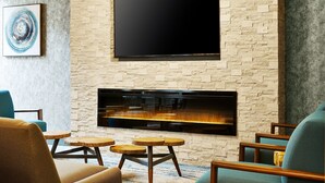 A modern living room with a stone wall, a flat-screen TV mounted above a fireplace, and a blue armchair. - Four Points by Sheraton Chicago Westchester/Oak Brook (Westchester)