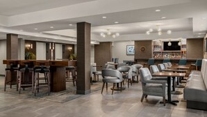 A modern hotel lobby with a bar area, seating arrangements, and a television screen. - Four Points by Sheraton Chicago Westchester/Oak Brook (Westchester)