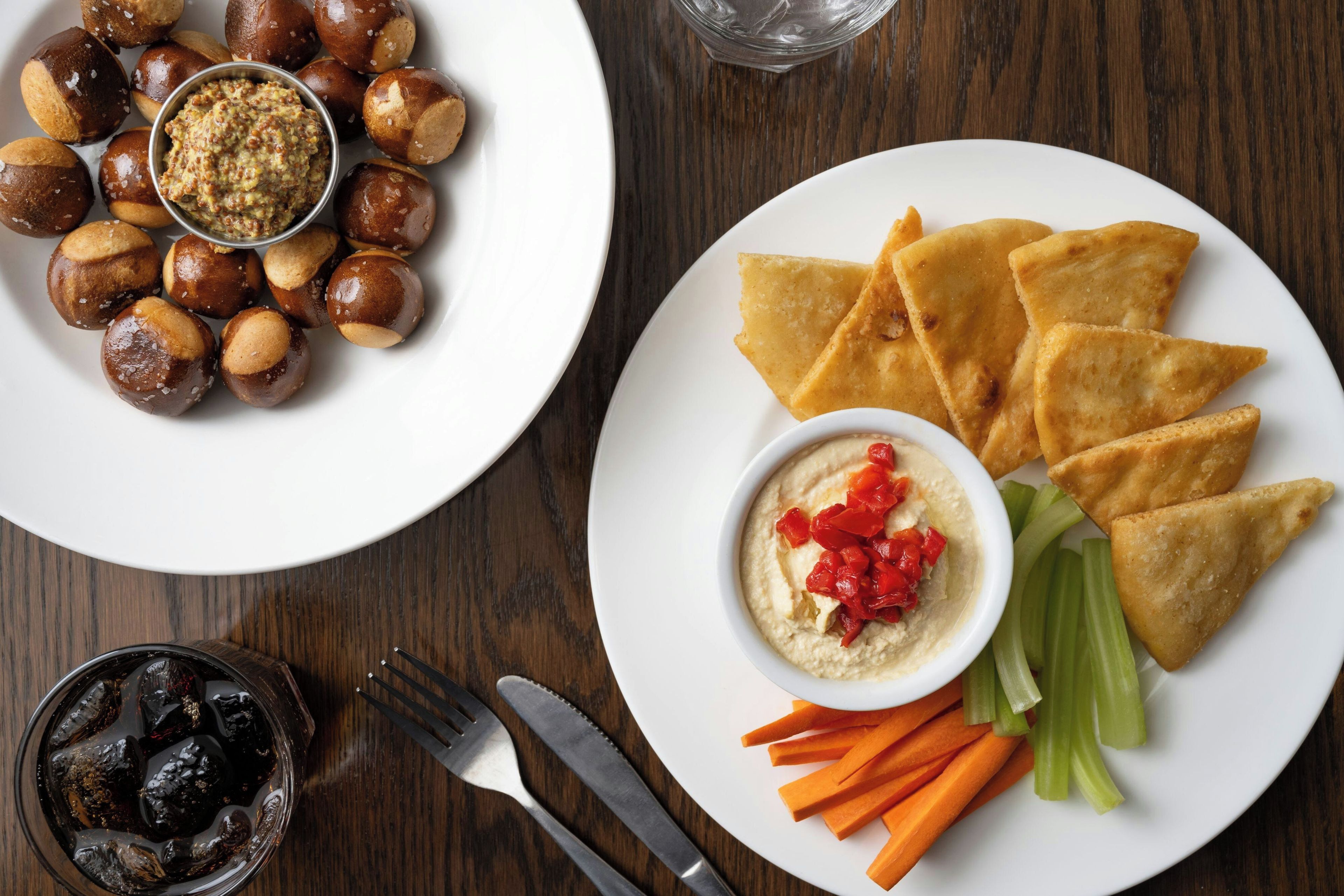 A dining table with plates of food, a bowl of dip, and a glass of soda.