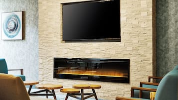 Una sala de estar con televisor de pantalla plana montado en una pared de piedra, una chimenea abajo y un sillón azul.