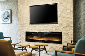 A living room with a flat-screen TV mounted on a stone wall, a fireplace below, and a blue armchair.