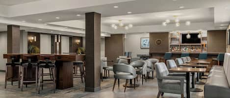 Un moderno vestíbulo de hotel con zona de bar, asientos y una pantalla de televisión.
