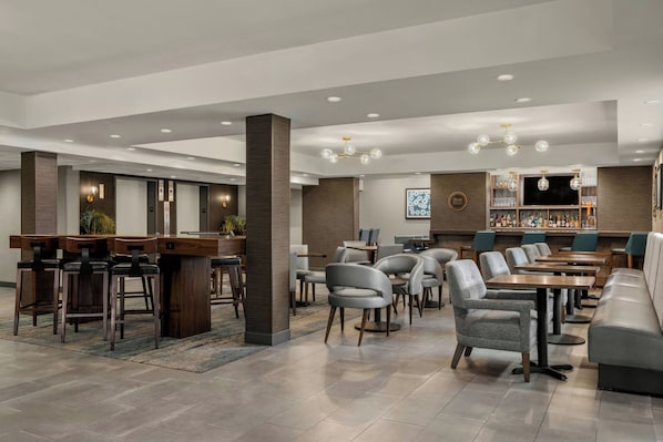A modern hotel lobby with a bar area, seating arrangements, and a television screen.