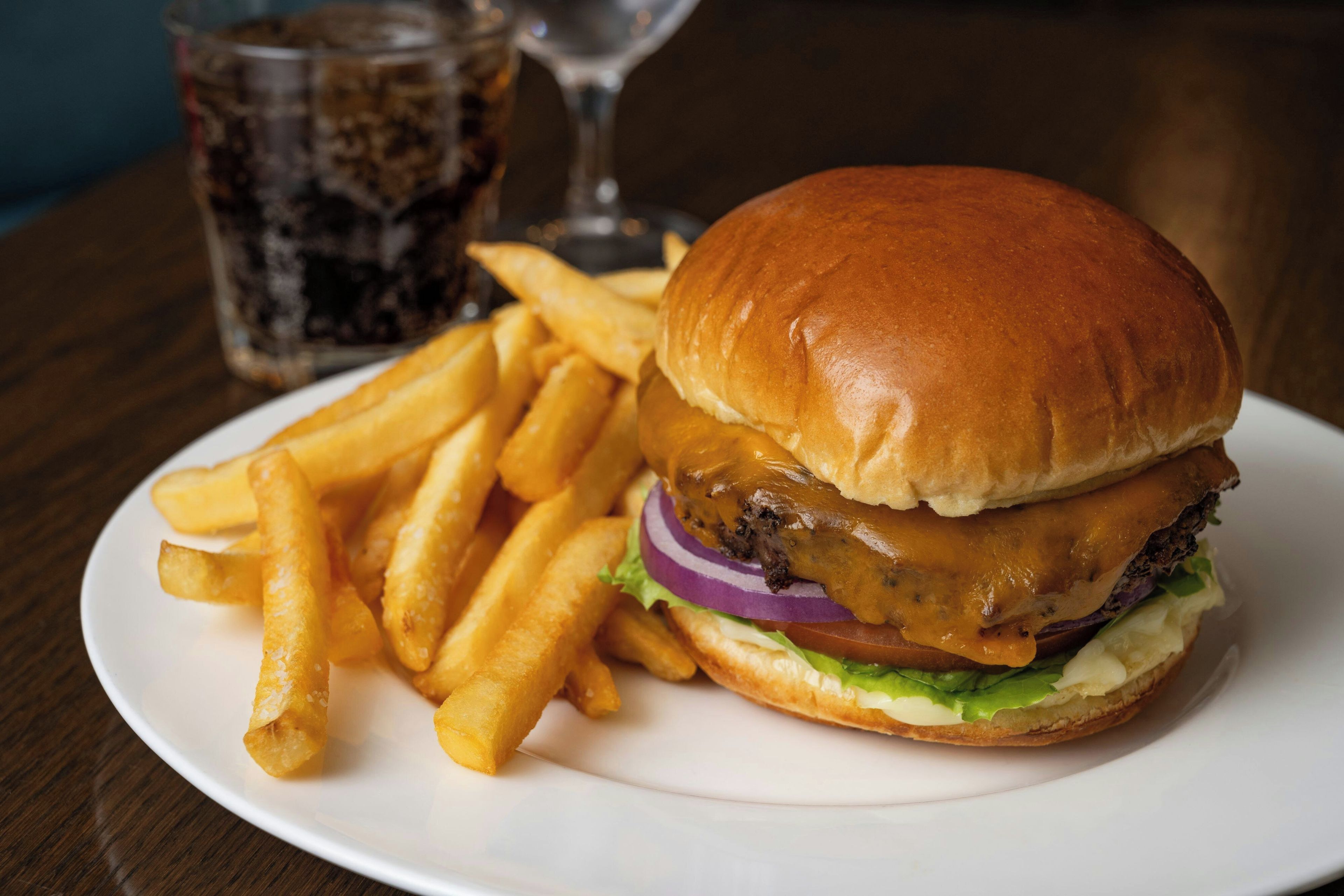 Ein Burger mit Pommes auf einem Teller, ein Glas Limonade und ein Glas Wasser auf einem Tisch.
