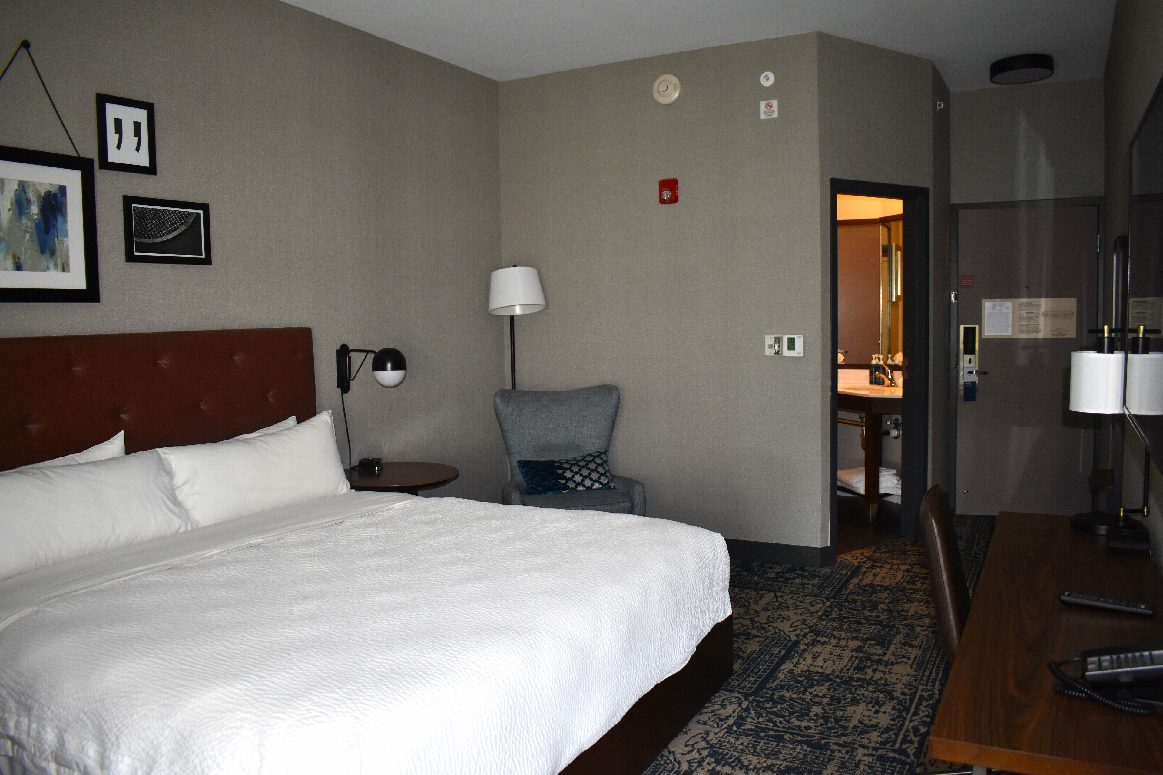 A hotel room with a large bed, a desk, a chair, a lamp, and a patterned rug.