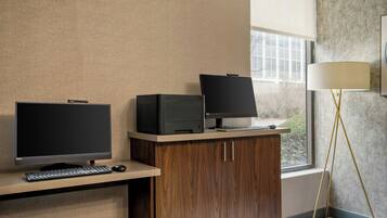 A hotel room with a desk, two monitors, a keyboard, a mouse, and a lamp.