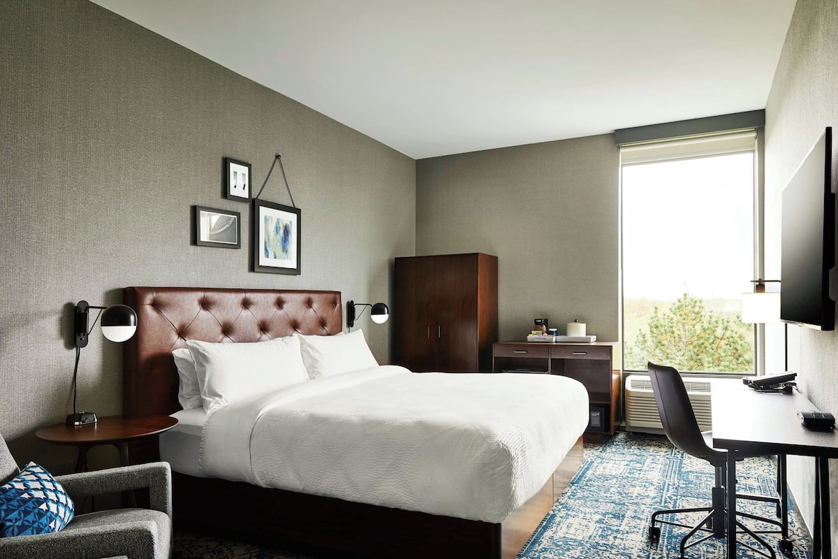 Een hotelkamer met een groot bed, een bureau, een stoel, een kledingkast en een televisie.